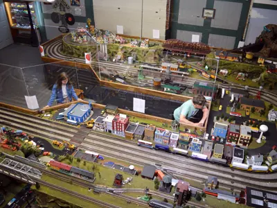 An overhead view of the NNYCRRM's O-gauge model train layout with kids watching model trains