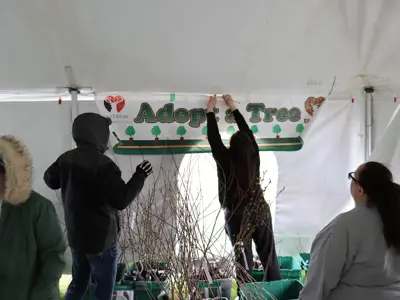 Volunteers hang Adopt-A-Tree banner at tree giveaway at Earth Day event at EEC